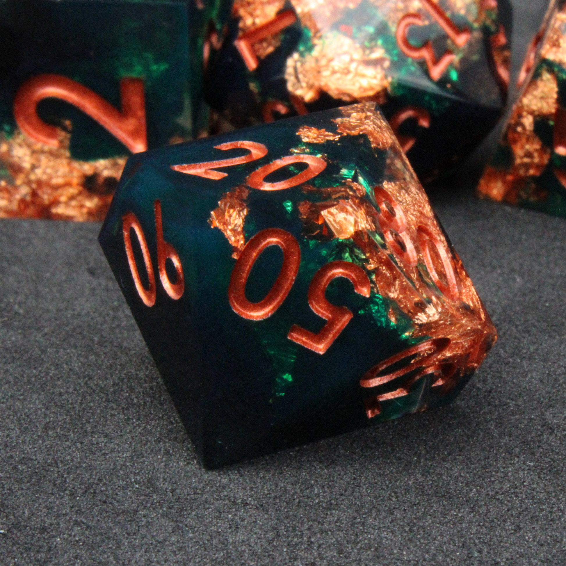Dark green and black resin sharp edge dice with copper flakes and glitter inside it. The polyhedral dice are used for tabletop roleplaying games like Dungeons & Dragons / DND / D&D and Pathfinder.