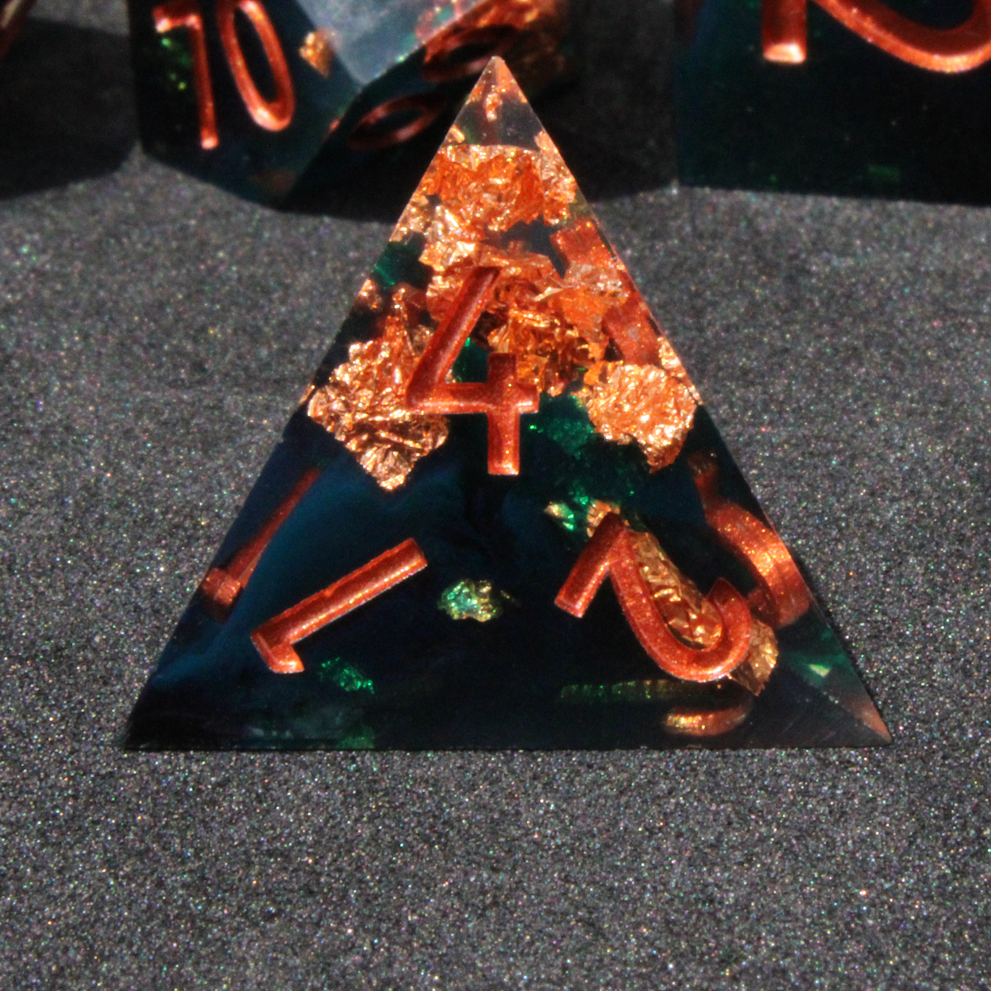 Dark green and black resin sharp edge dice with copper flakes and glitter inside it. The polyhedral dice are used for tabletop roleplaying games like Dungeons & Dragons / DND / D&D and Pathfinder.