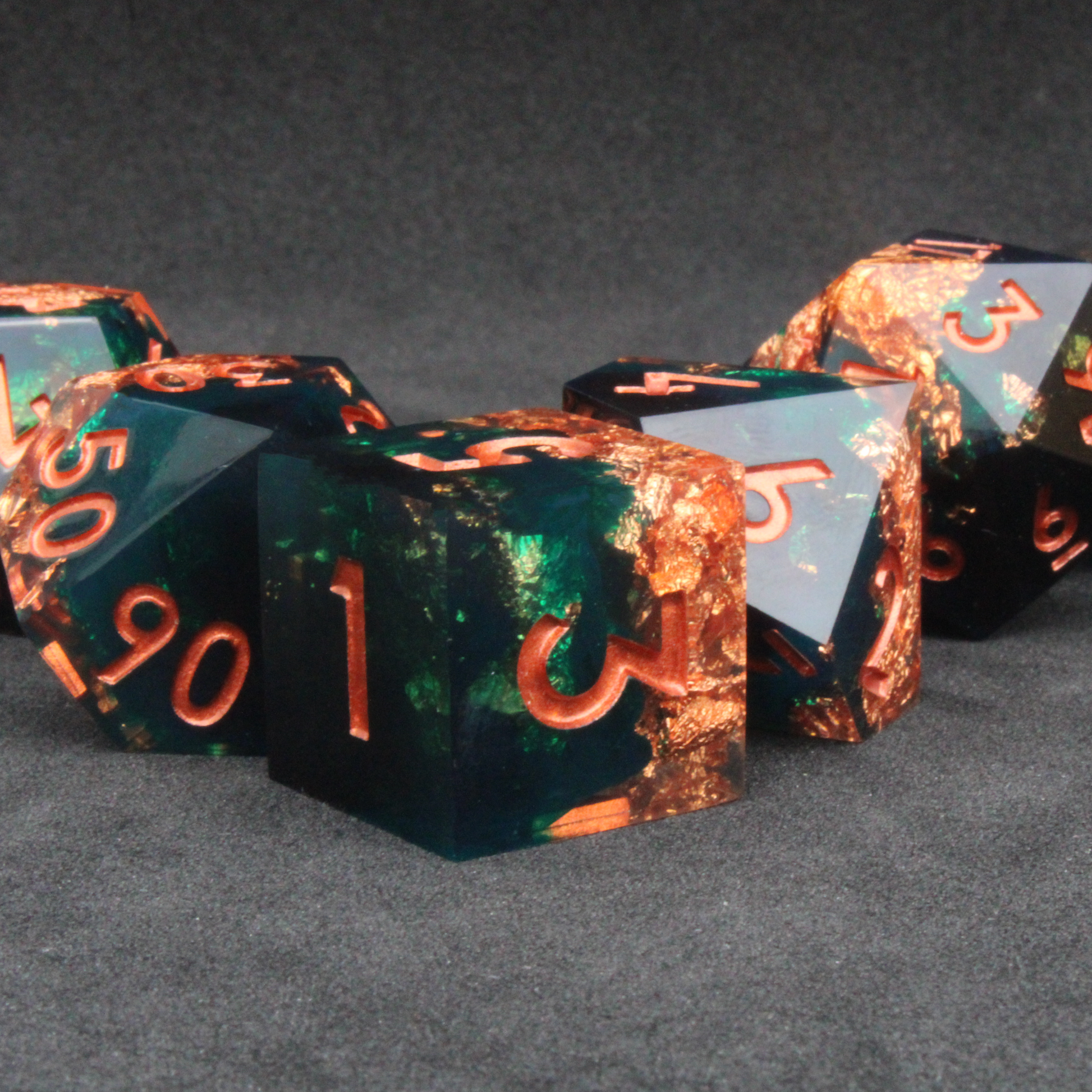 Dark green and black resin sharp edge dice with copper flakes and glitter inside it. The polyhedral dice are used for tabletop roleplaying games like Dungeons & Dragons / DND / D&D and Pathfinder.