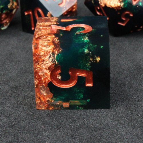 Dark green and black resin sharp edge dice with copper flakes and glitter inside it. The polyhedral dice are used for tabletop roleplaying games like Dungeons & Dragons / DND / D&D and Pathfinder.