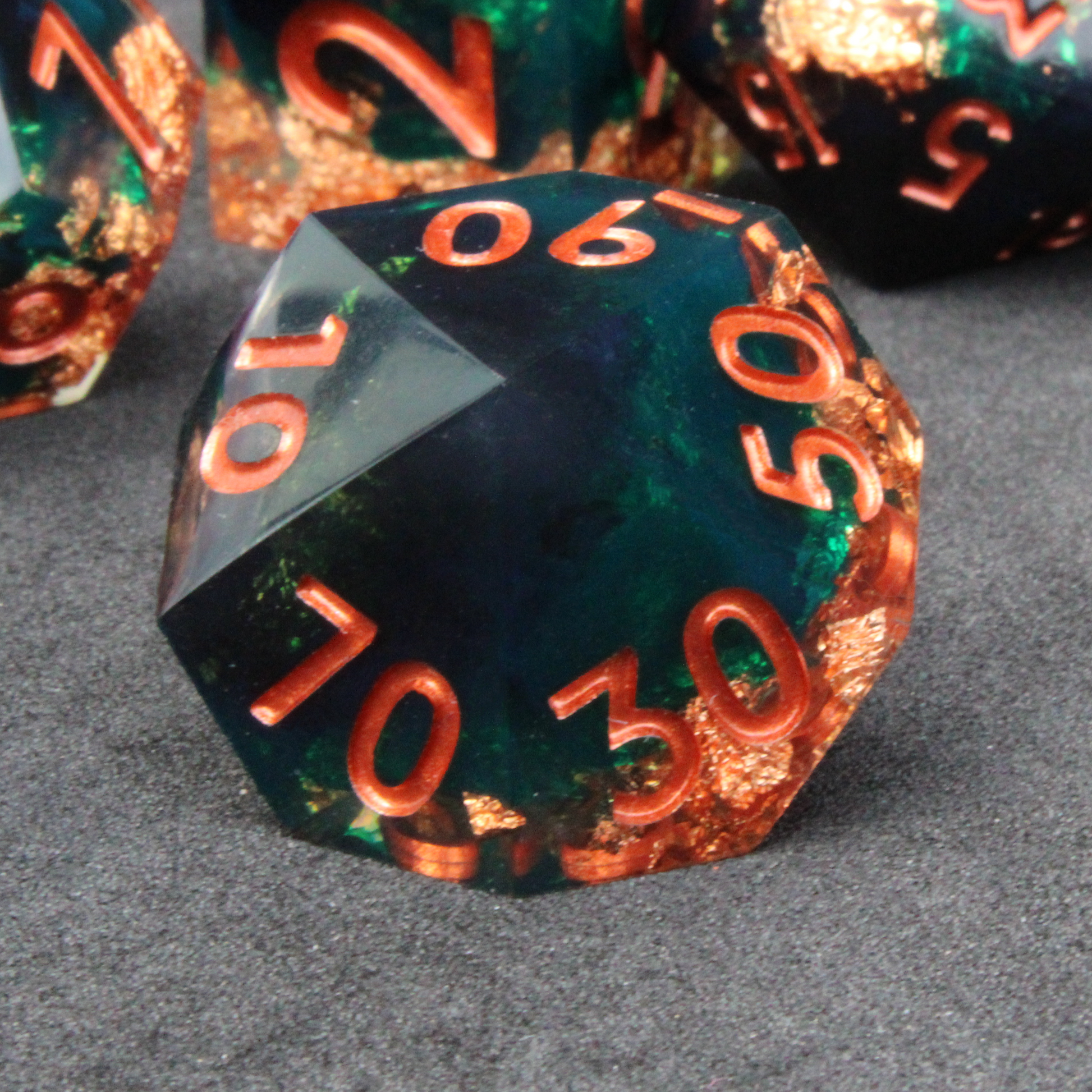 Dark green and black resin sharp edge dice with copper flakes and glitter inside it. The polyhedral dice are used for tabletop roleplaying games like Dungeons & Dragons / DND / D&D and Pathfinder.