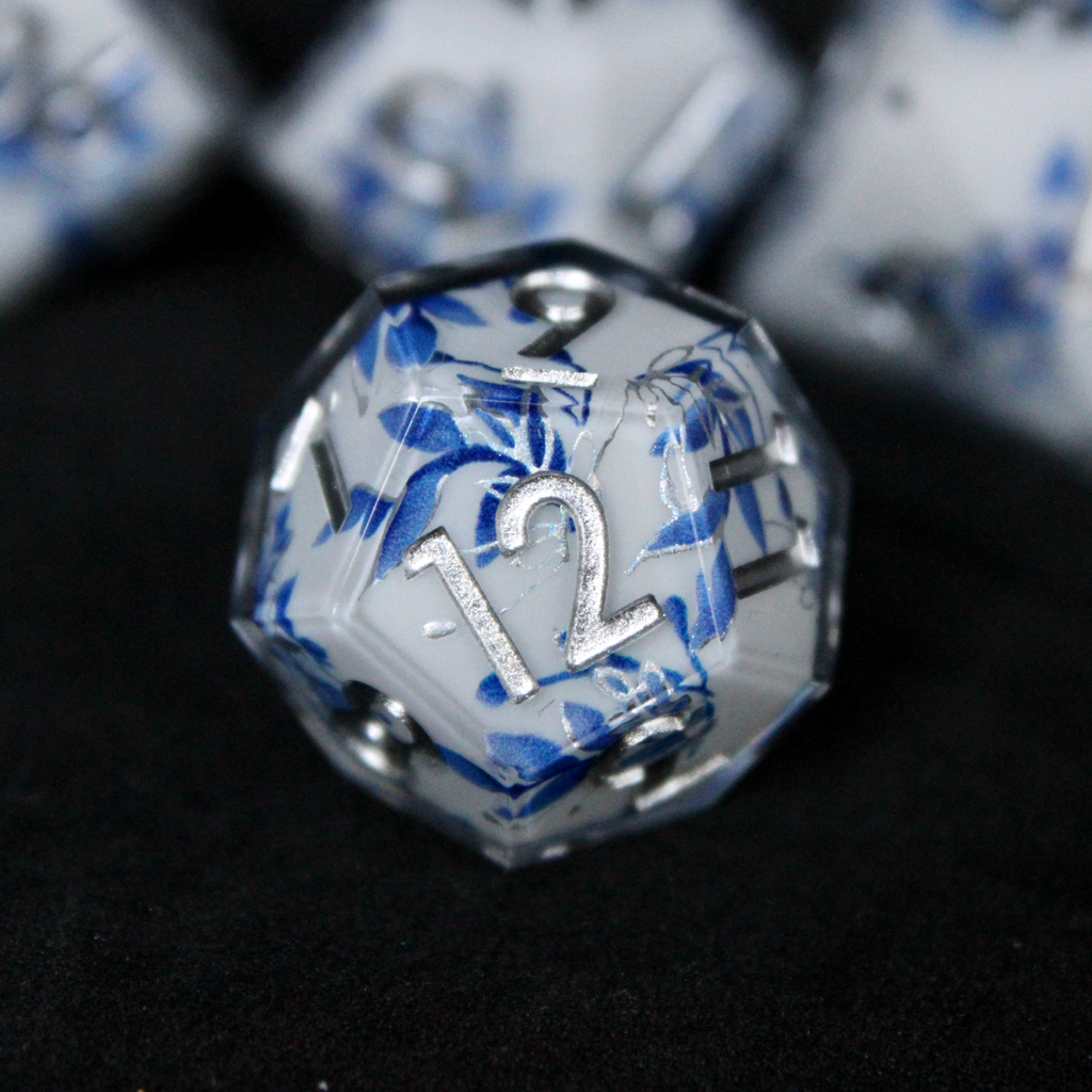 A bright white DND dice set with blue and silver flower patterns on it. The dice are used for TTRPGs like DnD / D&D / Dungeons & Dragons and Pathfinder. 