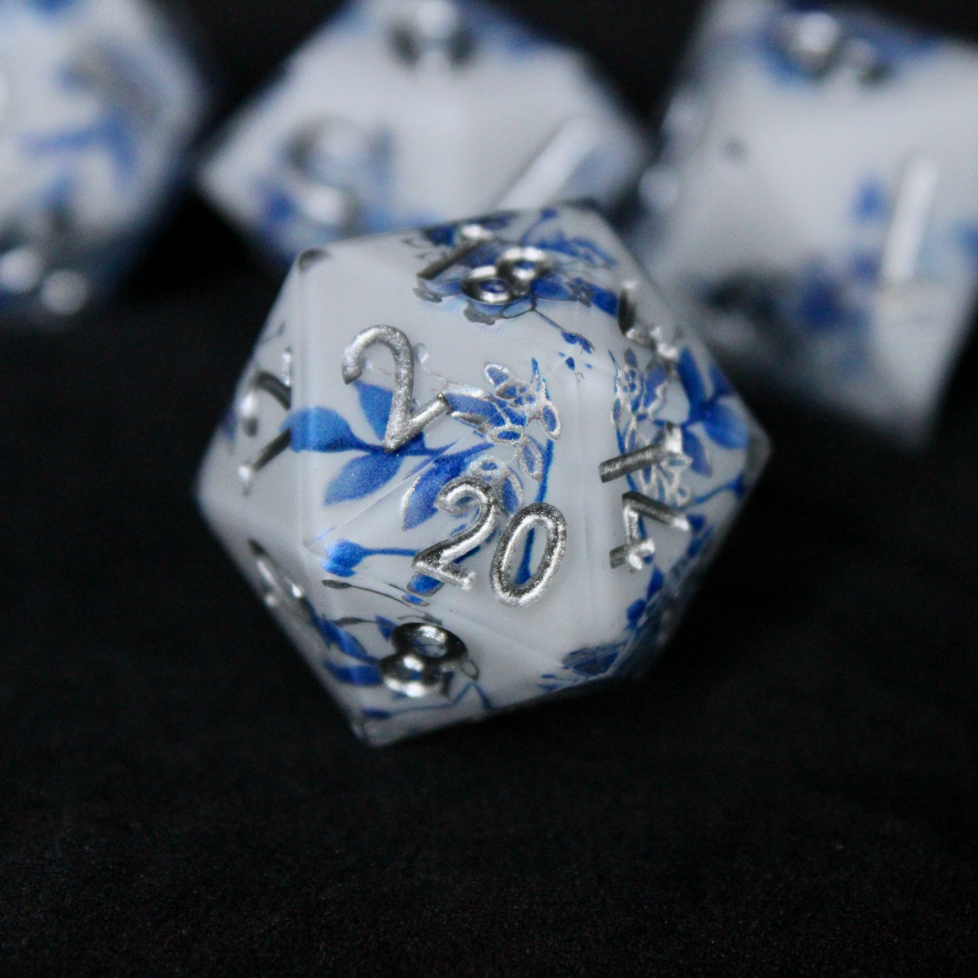 A bright white DND dice set with blue and silver flower patterns on it. The dice are used for TTRPGs like DnD / D&D / Dungeons & Dragons and Pathfinder. 