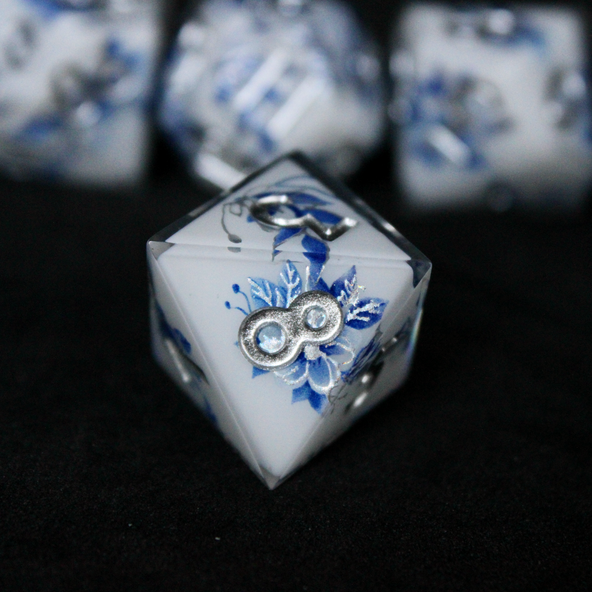 A bright white DND dice set with blue and silver flower patterns on it. The dice are used for TTRPGs like DnD / D&D / Dungeons & Dragons and Pathfinder. 