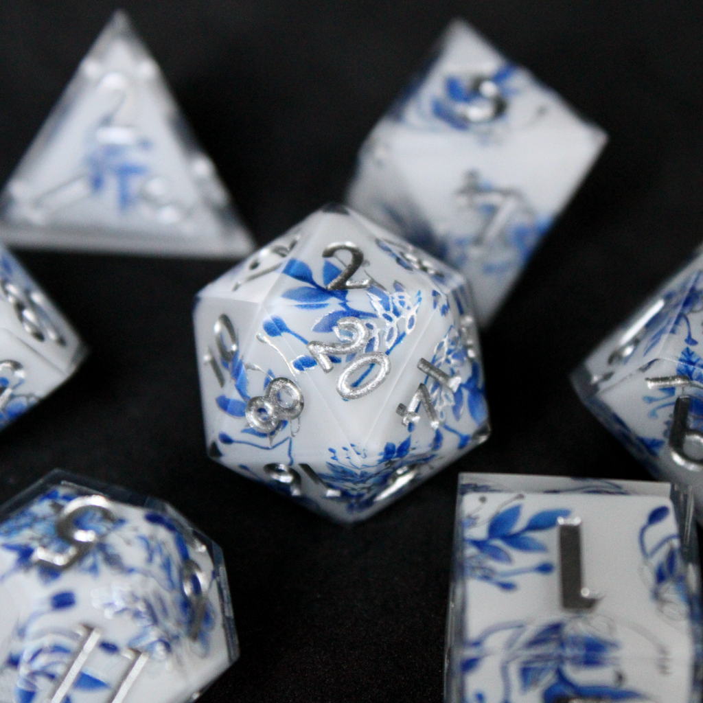 A bright white DND dice set with blue and silver flower patterns on it. The dice are used for TTRPGs like DnD / D&D / Dungeons & Dragons and Pathfinder. 