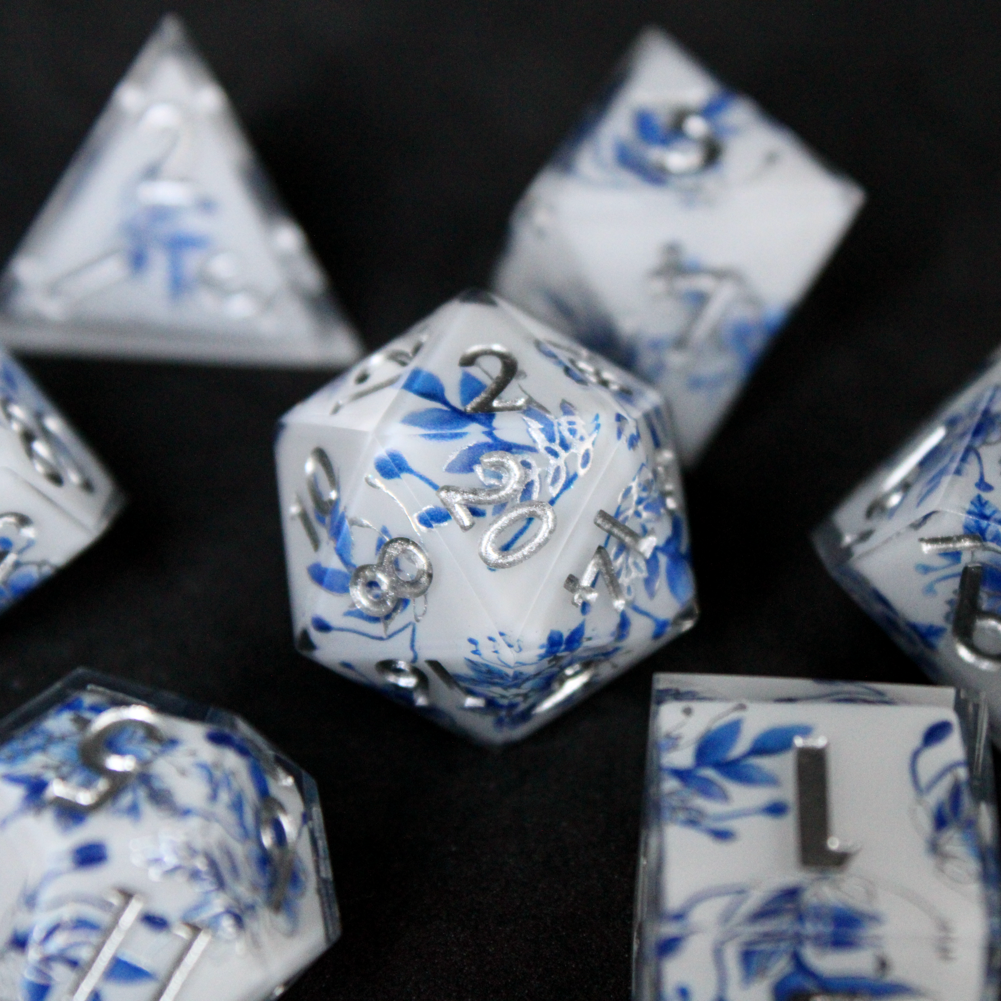A bright white DND dice set with blue and silver flower patterns on it. The dice are used for TTRPGs like DnD / D&D / Dungeons & Dragons and Pathfinder. 