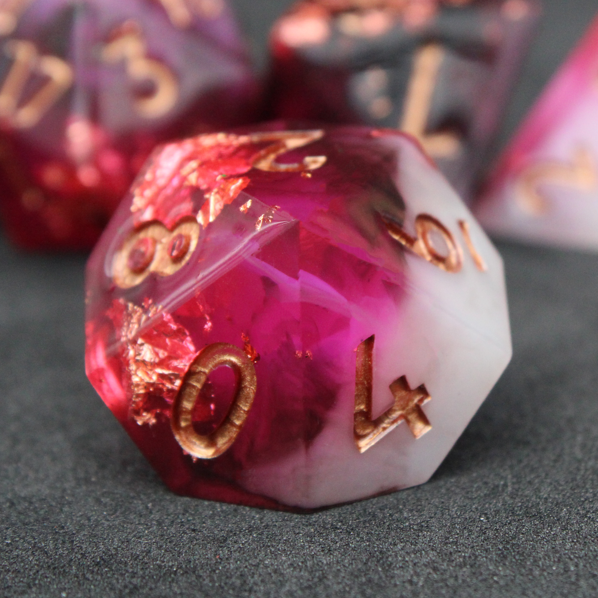 Black, pink and red resin sharp edge dice. These polyhedral dice are used to play TTRPGs like Dungeons & Dragons / D&D / DND and Pathfinder.