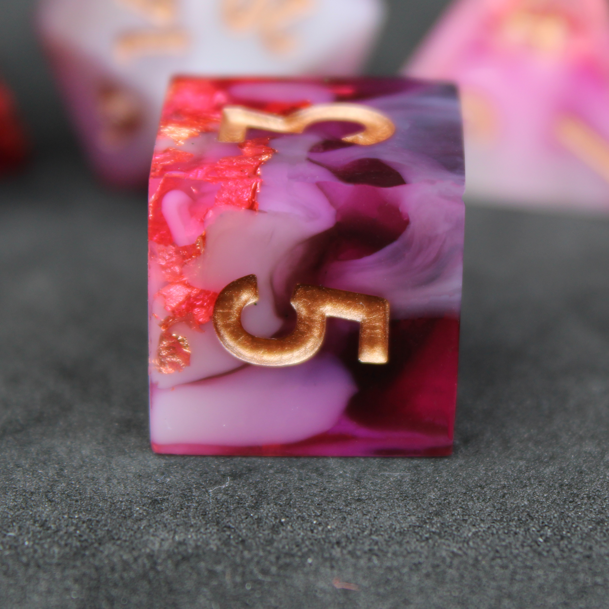 Black, pink and red resin sharp edge dice. These polyhedral dice are used to play TTRPGs like Dungeons & Dragons / D&D / DND and Pathfinder.