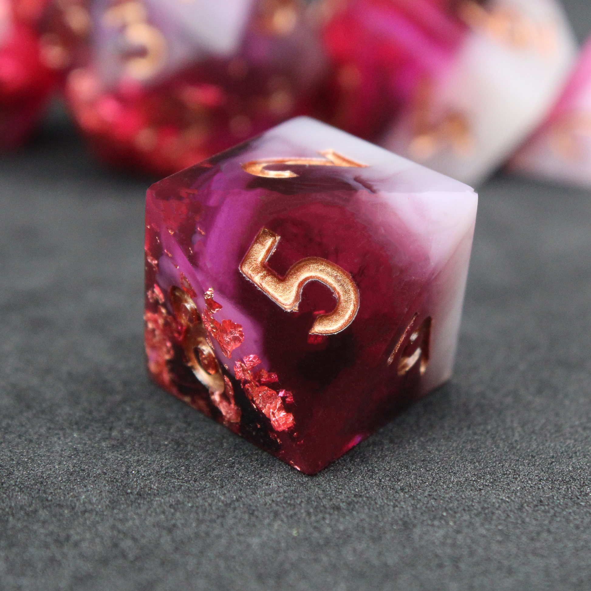 Black, pink and red resin sharp edge dice. These polyhedral dice are used to play TTRPGs like Dungeons & Dragons / D&D / DND and Pathfinder.